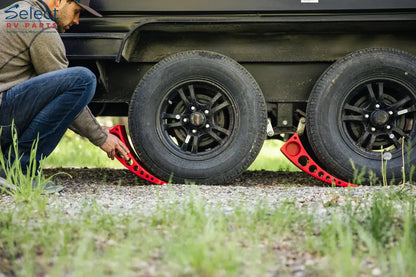 Person using a tire jack to lift a vehicle tire on a gravel surface.