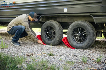Person using red tire levers on a trailer tire on a gravel surface