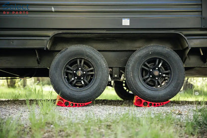 Close-up of a trailer with black tires on red tire guards in a grassy area.