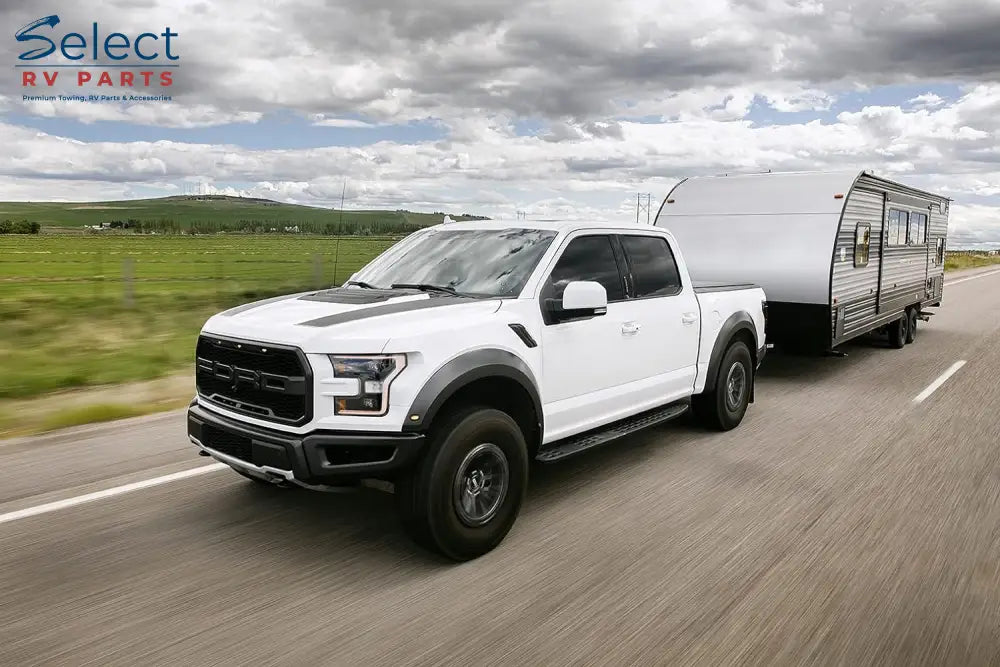 White pickup truck towing a camper on a road with a cloudy sky.