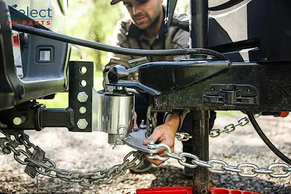 Person attaching a chain to a vehicle's hitch with a blurred natural background